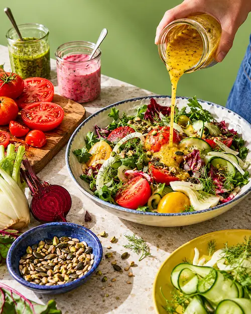 An overhead arrangement of small bowls holding dressings, herbs, seeds and vegetables like a flavour laboratory