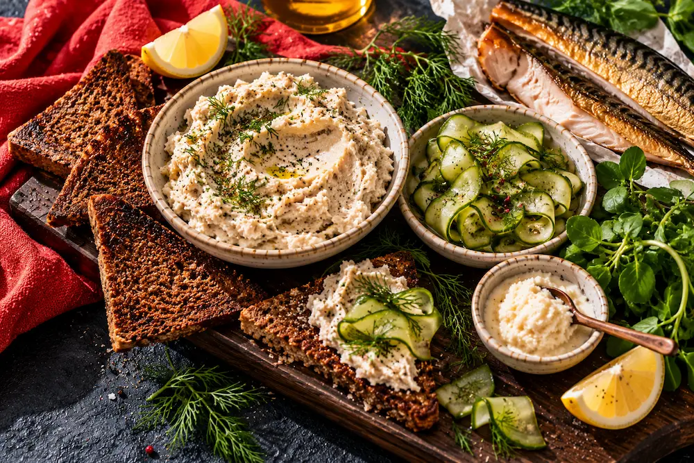 A creamy smoked mackerel pâté in a dish with dark rye toast, ribbons of pickled cucumber, lemon and dill