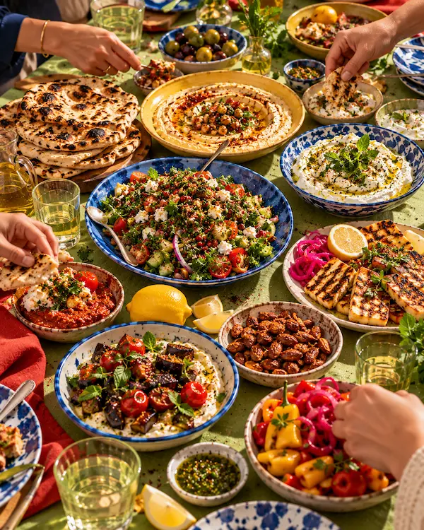 A long table loaded with mezze: flatbreads, dips, herb salad, spiced nuts and griddled halloumi