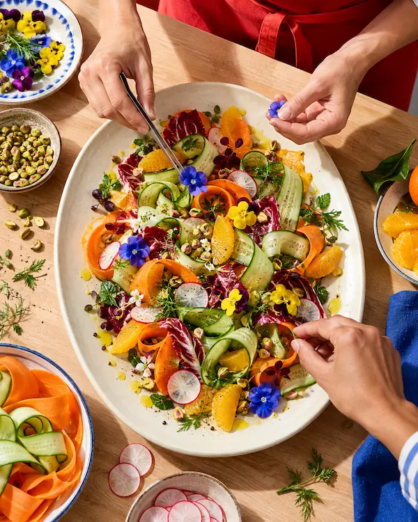 Hands arranging a colourful salad on a large platter during a cooking class